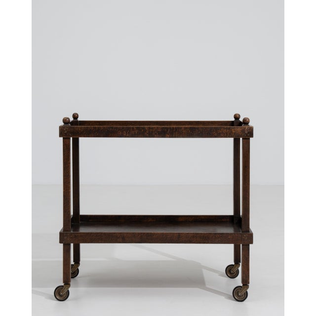 A circa 1960 French bar cart constructed in wood, featuring a rectangular frame with open shelving and mounted on casters....