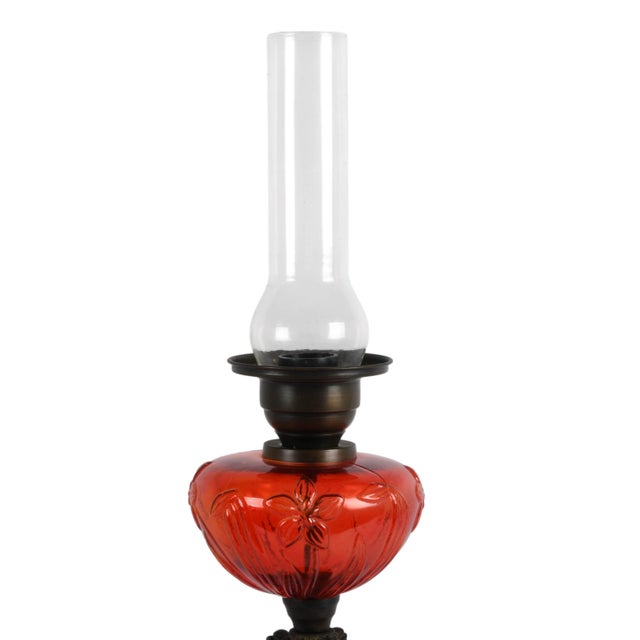 This antique Victorian ruby red glass oil lamp features a richly colored pressed glass reservoir adorned with ornate...