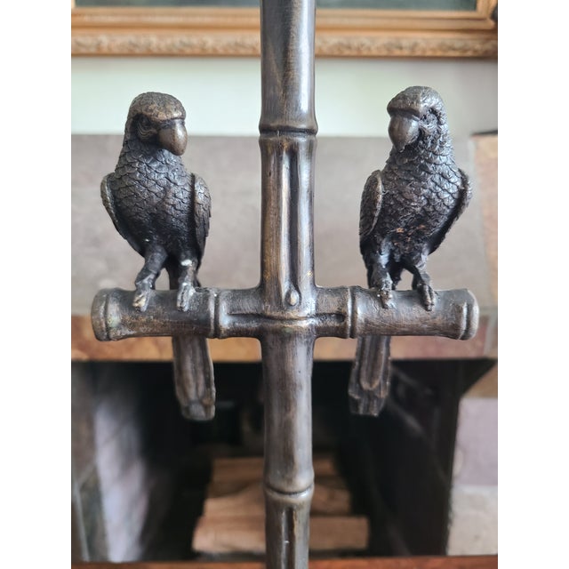 Rare 1940s table lamp featuring a pair of bronze parrots perched on a branch of faux bamboo. It casts a warm, inviting...