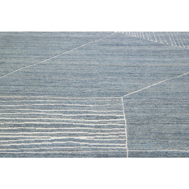 This luxurious wool rug features a timeless Moroccan pattern in a contemporary abstract Minimalist style, utilizing blue...