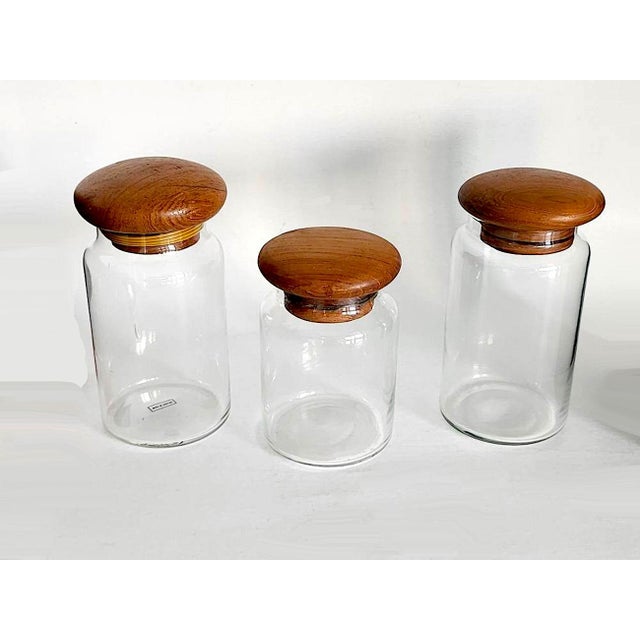 Offered is a set of 3 medium sized glass canisters with teak wood lids. The lids had/have rubber stopper rims to help them...
