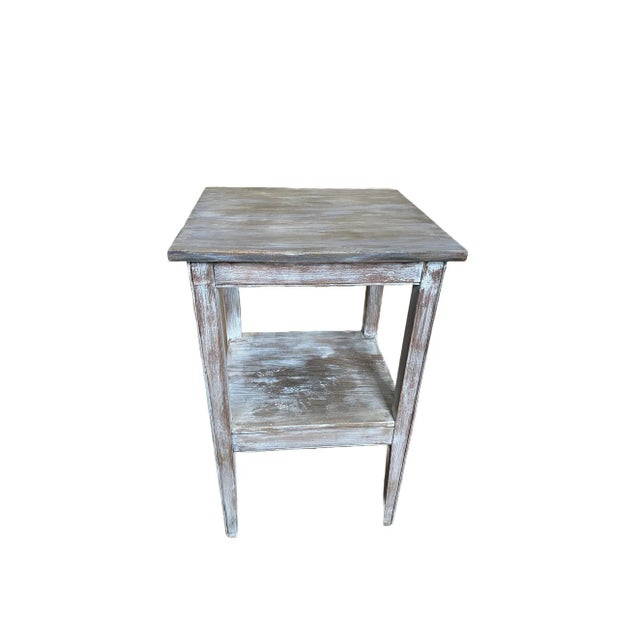 A painted distressed side table that is white and grey with some accents of brown. This side table is from the 1950's and...