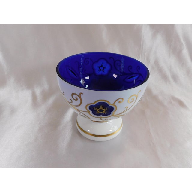 This is a white over blue cut to clear bowl that has a white bottom and no markings. It has a simple gold design with gold...
