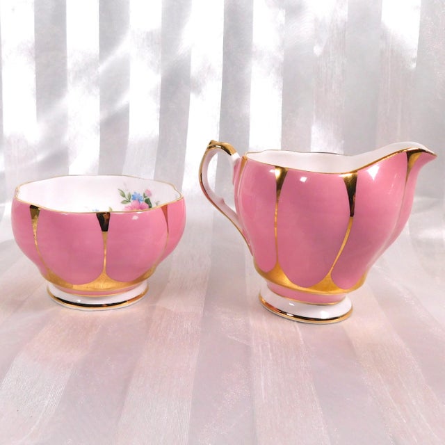 This is a Queen Anne (England) Bone China sugar bowl and creamer in bright pink and gold with a floral design on the...