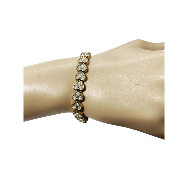 Vintage gold tone tennis bracelet featuring pave rhinestone heart accents. Measures 7.25" long with a delicate 0.25" width...