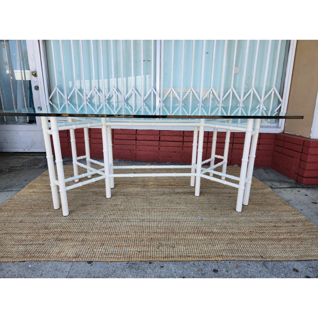 Elegant dining table with a white bamboo Style Wood base and a thick rectangular glass top. The base has a geometric...