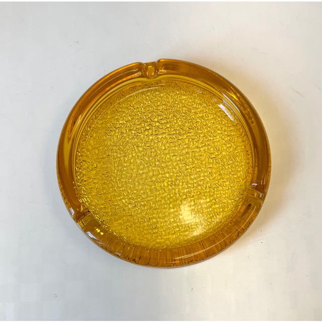 A warm amber colored glass ashtray, with pebbled textural base. C.1970's. Dimensions: 7 1/8"diameter x 1 1/8"H