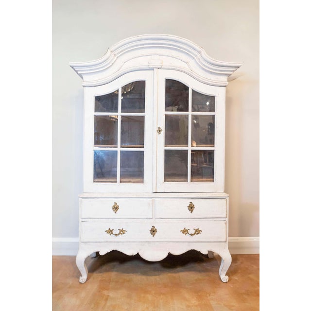 A Swedish period Rococo painted wood cabinet with bonnet-shaped pediment, glass doors, lower drawers and original hardware...