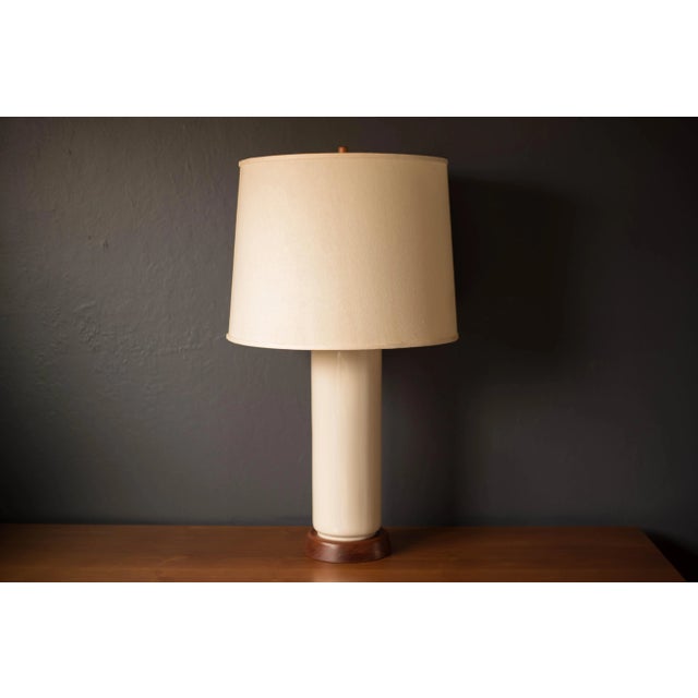 Mid-century modern white cylinder table lamp, circa 1950s. This sculptural piece is accented with a walnut base and...