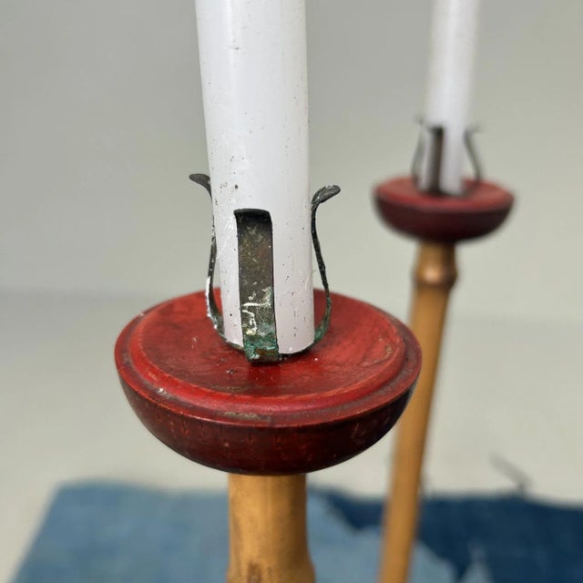 A refined pair of tall, slender candlesticks with bamboo shafts and deep chestnut-red lacquered bases and cups. At the top...