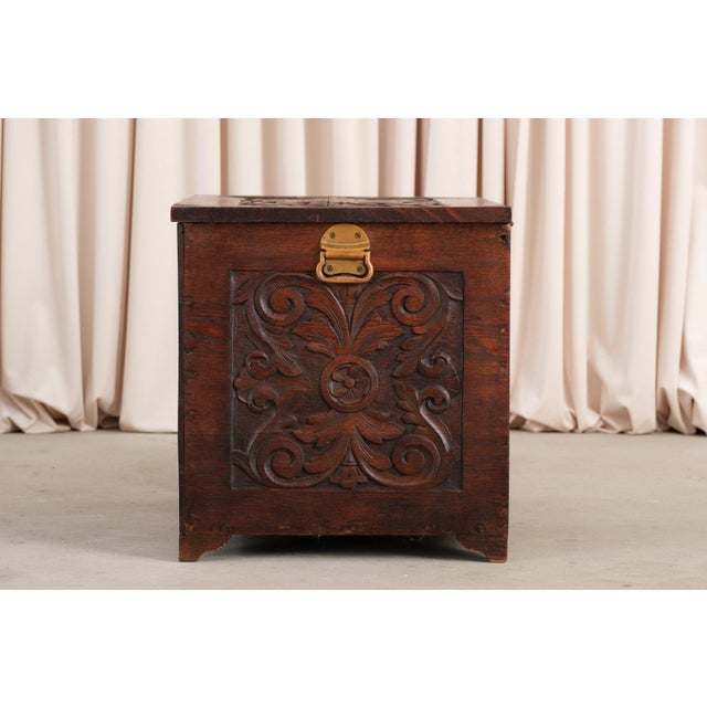 A carved oak chest in the Jacobean Revival style. The front panel has scrolling acanthus leaves around a central oval...
