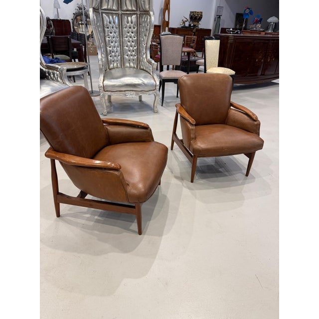 A pair of mid century modern leather club chairs in the manner of Finn Juhl with floating arms and turned and tapered legs...