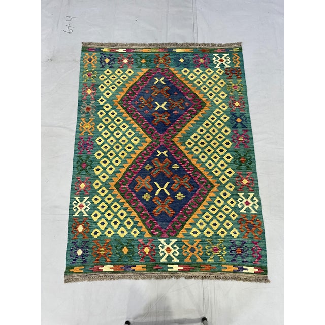 This Afghan Chobi wool kilim features a rich teal green field with two navy blue diamond medallions, surrounded by...