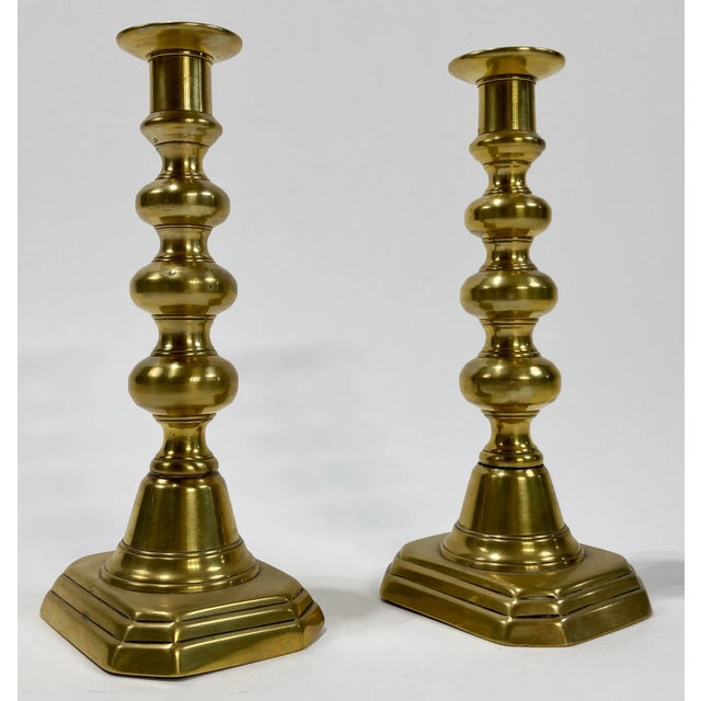 Decorative pair of antique English style brass push-up style candlesticks. Feature detailed shaft and squared bases. A...