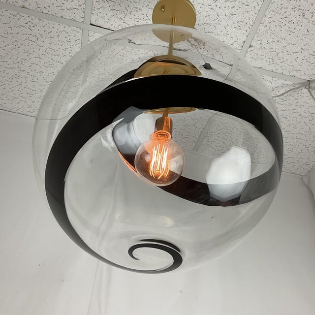 A striking contemporary pendant light featuring a large handblown smoked glass globe accented b a dramatic black spiral...