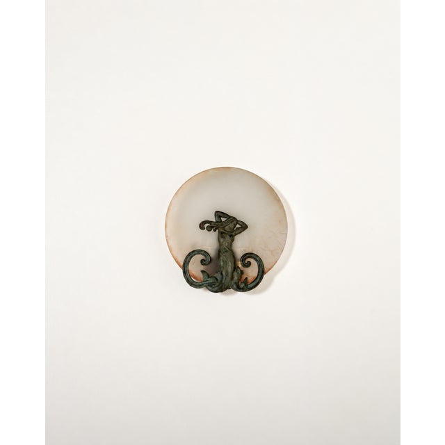 Patinated metal wall light with a female figure and ornamental scroll motifs, complemented by a circular frosted glass...