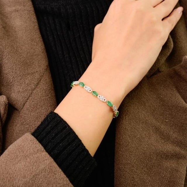 This elegant tennis bracelet features oval-cut natural emeralds totaling 3.55 carats, beautifully set in 18K yellow gold....