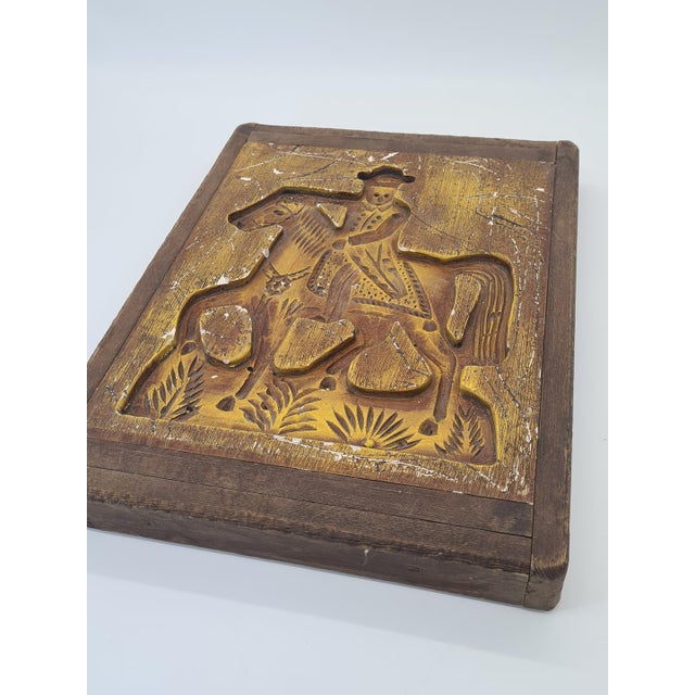 A unique, antique wooden model featuring a deeply carved depiction of a rider on horseback, set in a sturdy wooden frame....