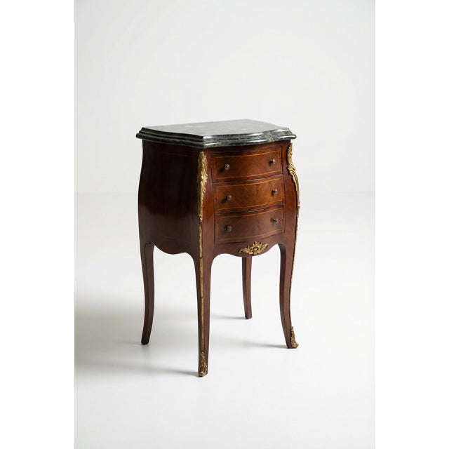 Elegant and richly detailed, this French Louis XV-style rosewood marquetry bombe nightstand bedside table features a...