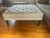Stylish and versatile upholstered ottoman featuring a soft, neutral fabric with a subtle blue geometric pattern. The...