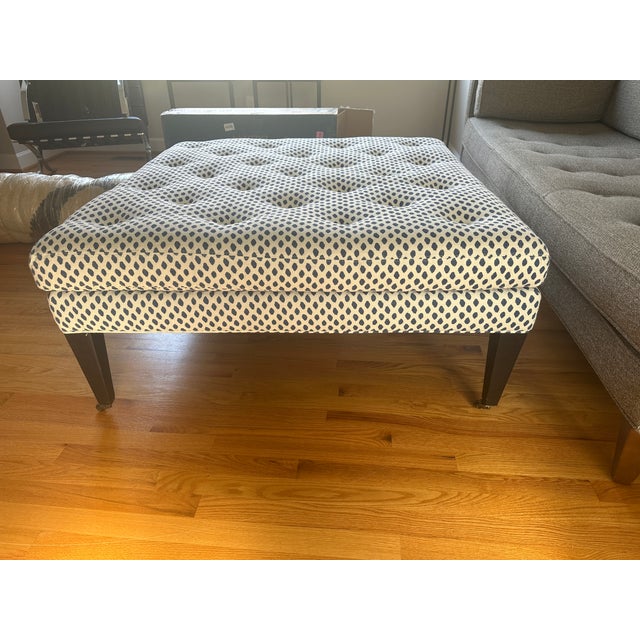 Stylish and versatile upholstered ottoman featuring a soft, neutral fabric with a subtle blue geometric pattern. The...