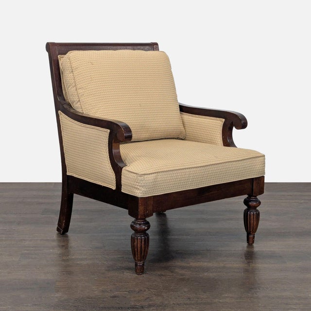 This lounge chair features a sturdy wood frame with carved legs and curved arms. The chair has soft beige cushions for...