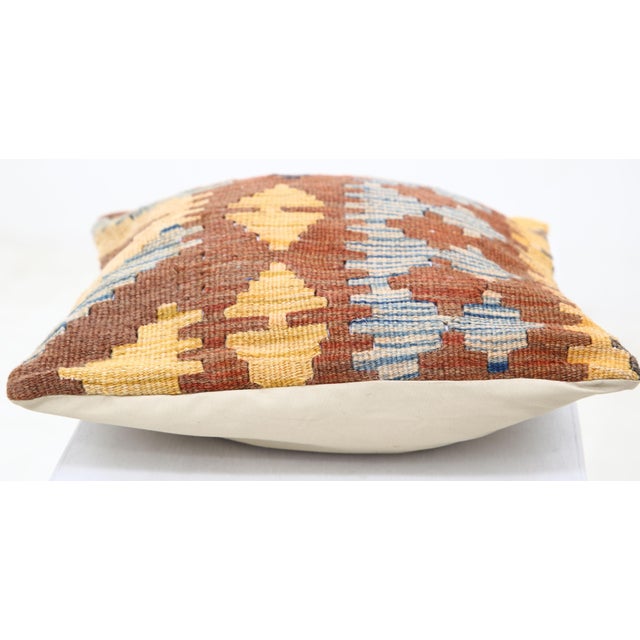 A one-of-a-kind handwoven Afghan wool kilim accent pillow featuring banded zigzag and diamonds on a rust ground. Cut and...