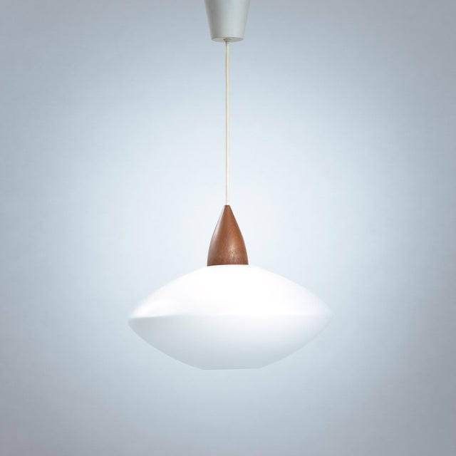 This beautiful ufo pendant light in opaline glass with teak in great condition was designed and produced by Swedish...