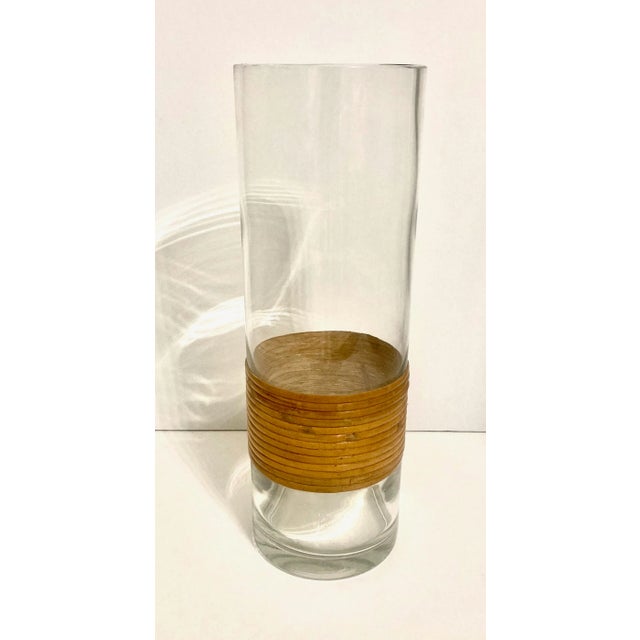 Cylindrical glass vase designed with a burnt rattan sleeve. This translucent piece is quite substantial, being a quarter...