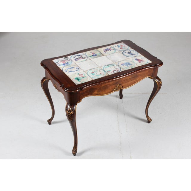 Danish Rococo-style table made of mahogany with curved legs and gilded carvings of stylized foliage. The tiles are...