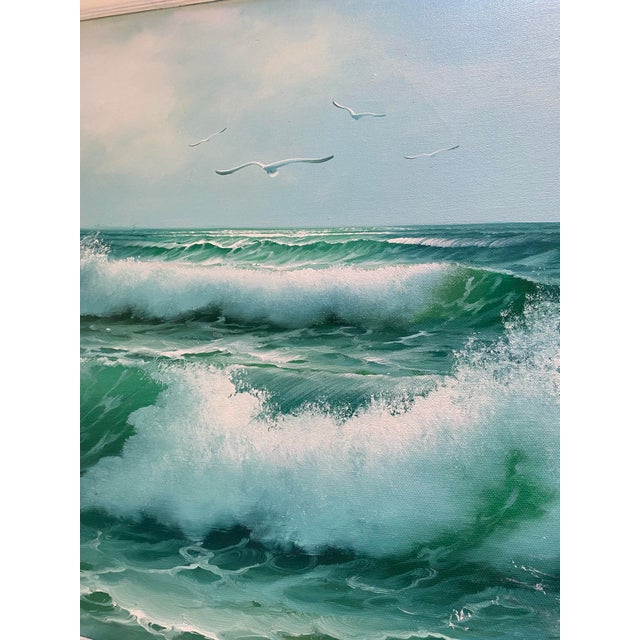 A large, atmospheric seascape oil painting capturing crashing turquoise waves beneath a soft blue sky dotted with...