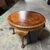 A decorative round Art Deco-style coffee table with a dramatic bookmatched burr walnut top, carved pie-crust edge and...