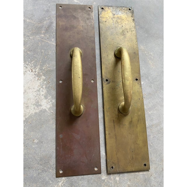 Primitive unlacquered brass cast brass door pulls attached to long, slim backplates. These have a patinated finish that...