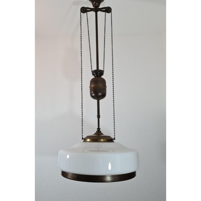 An original pendant lamp from the Art Deco period, made of patinated brass and a milky opal glass shade. A classic,...