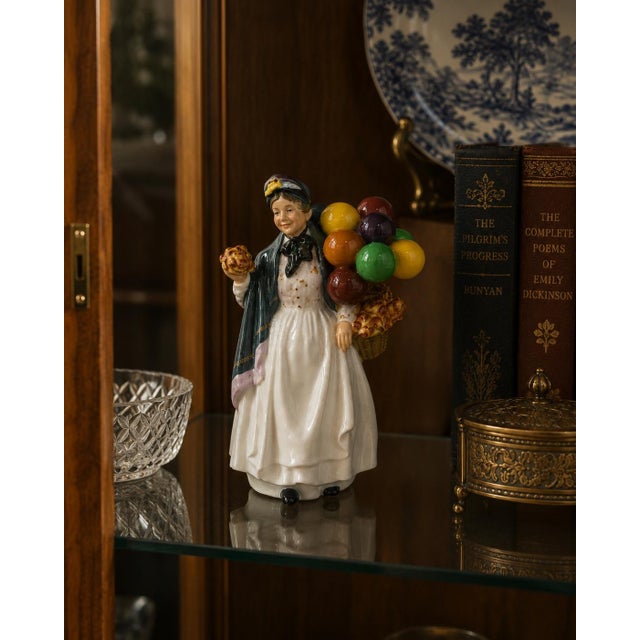 A delightful Royal Doulton “Biddy Penny Farthing” figurine (HN 1843) depicting a cheerful street vendor carrying a bundle...