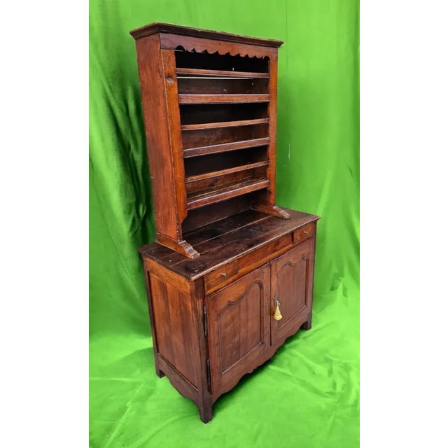 This 18th-century French Country Vaisselier is a charming antique collectible crafted from rich wood that has developed a...