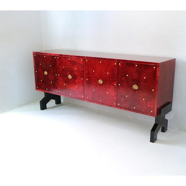 Sideboard with four doors, wooden structure covered with red parchment, base with black lacquered feet and golden handles....