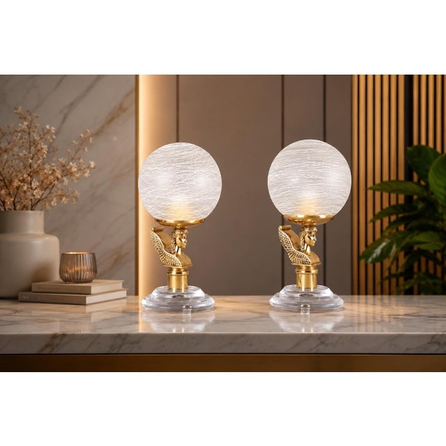 Pair of decorative table lamps dating to the 1980s. Each features a brass-toned winged bust supporting a textured frosted...