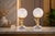 Pair of decorative table lamps dating to the 1980s. Each features a brass-toned winged bust supporting a textured frosted...