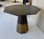 Sculptural octagonal pedestal table featuring a faceted wood top and a geometric base clad in brass. The design balances...