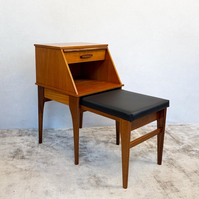 Constructed in teak, with an angled box unit sitting above an underframe incorporating a sliding newly upholstered seat....