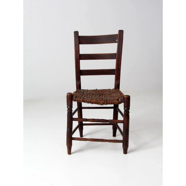 This antique splint weave seat chair features a rustic wooden frame with a classic ladder-back design. The seat is...