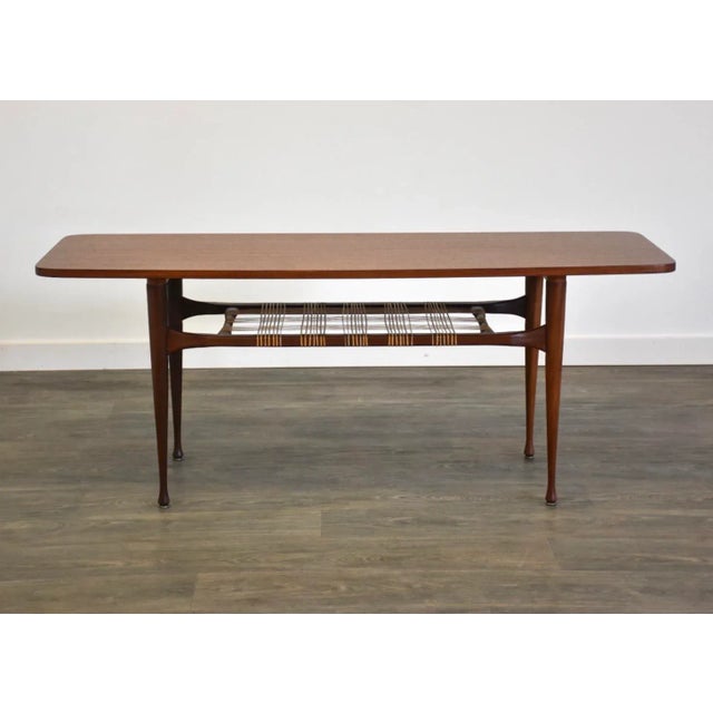 A mid century modern tall teak coffee table with a lower cane magazine shelf. Professionally refinished. Unmarked. 56.25”...
