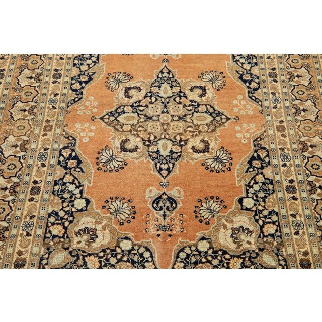 This Persian Tabriz wool rug showcases an exquisite traditional floral medallion design with a striking tan accent against...