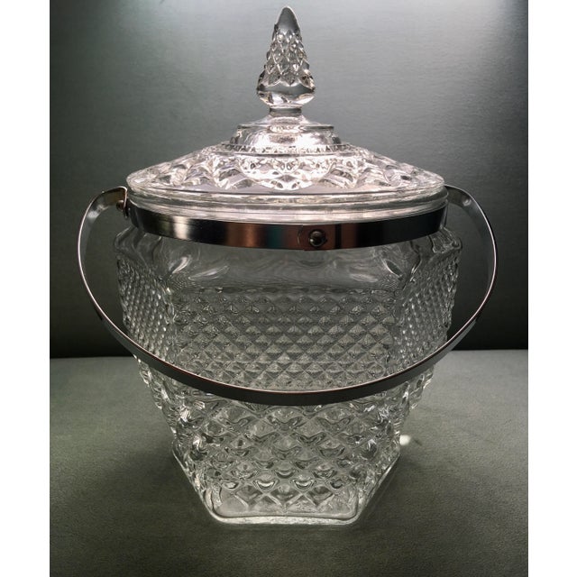 A vintage chrome handled glass ice bucket in a textured pattern with a wider diamond band at the bottom and a smaller...