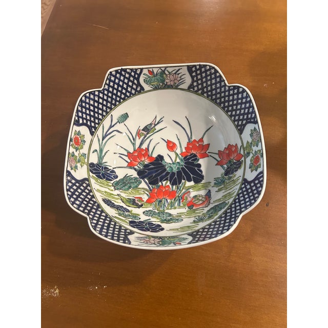 The bowl features a detailed hand-painted lotus garden scene with birds, accented in classic Imari Hues of deep cobalt...