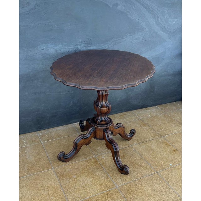 Early 20th-century Victorian tilt-top pedestal table featuring a rotating circular top with a finely scalloped edge. The...