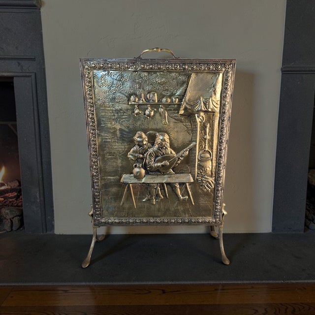This antique brass fireplace screen features a stamped repousse design with a tavern scene, adding a touch of vintage...
