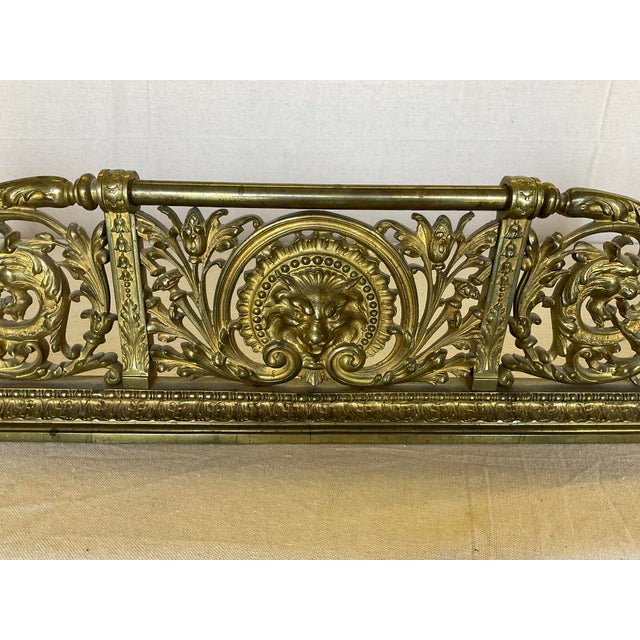 Fine Antique Lions Head Brass Fireplace Fender with Acorn Finials in good estate condition. It has an ornate, pierced...