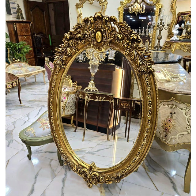 Elegant French-style oval wall mirror featuring an exquisitely hand-carved wooden frame with intricate floral and scroll...